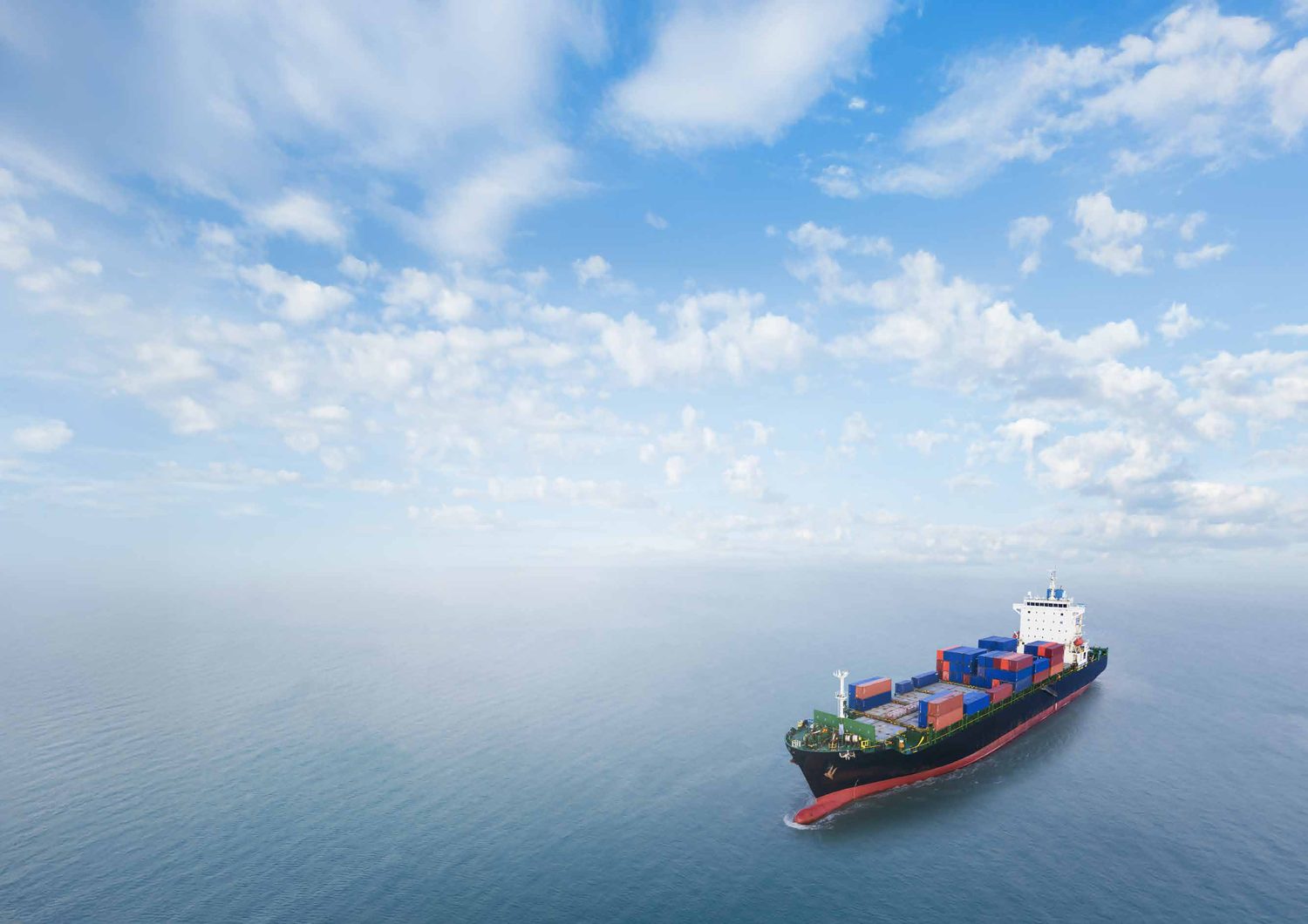 A container ship sailing across calm open ocean under a cloudy sky